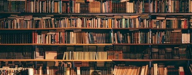 An image of multiple crowded shelves of books in a dimly lit library